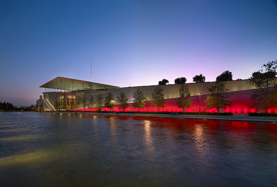 Φωτογραφία που δείχνει μια λίμνη στο τέλος της οποίας υπάρχει ένας τοίχος που φωτίζεται και την άκρη φαίνεται ένα μεγάλο γυάλινο κτήριο 