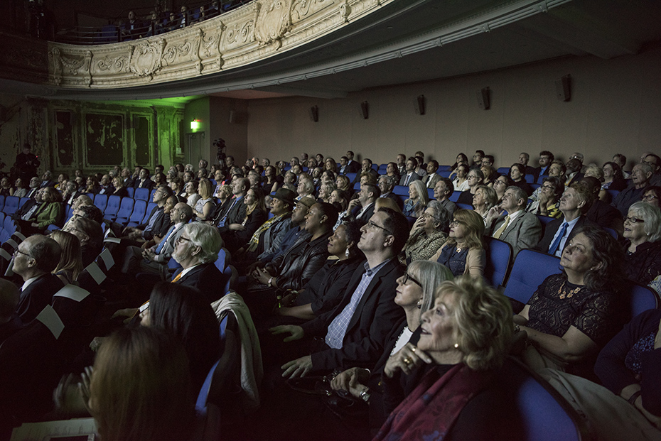 Φωτογραφία που δείχνει το κοινό να κάθεται σε καρέκλες θεάτρου και να παρακολουθεί την εικόνα που προβάλλεται