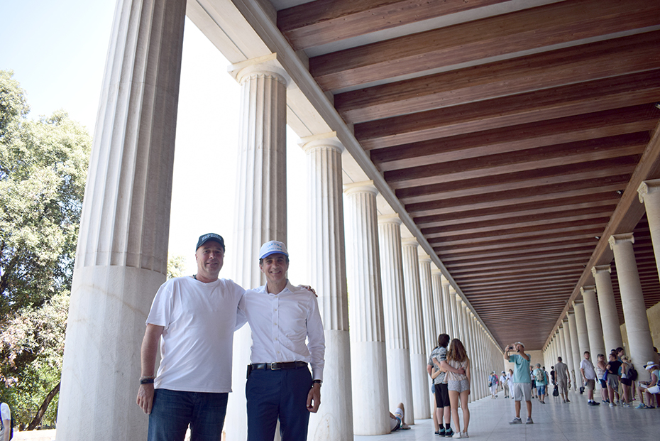 Ο Ανδρέας Δρακόπουλος και ένας άλλος άνδρας χαμογελούν μπροστά από στήλες σε αρχαιολογικό μουσείο