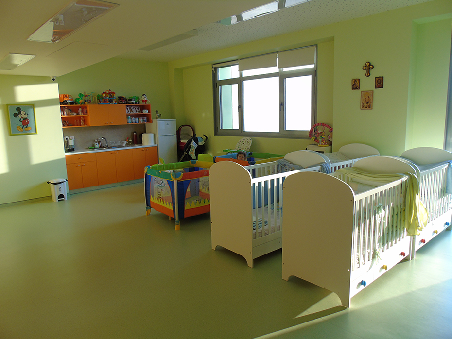 Φωτογραφία από το εσωτερικό ενός δωματίου το οποίο έχει έξι μωρουδιακές κούνιες και μια μικρή κουζίνα 