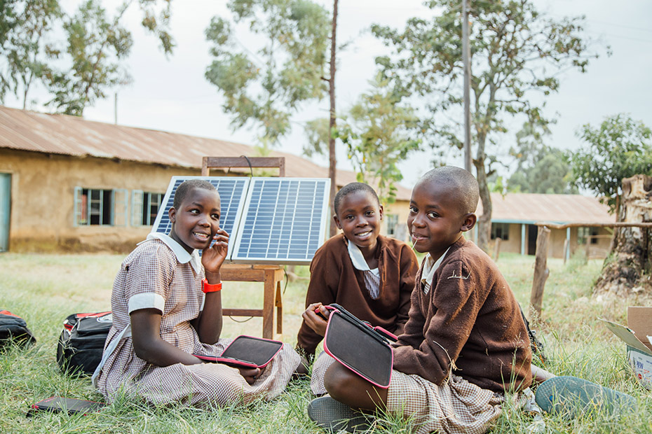Τρία παιδιά από την Κένυα κάθονται στο γρασίδι και χρησιμοποιούν τα ταμπλετ τους