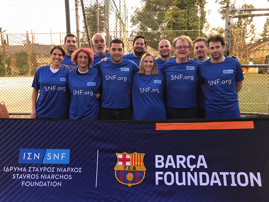 Μια ομάδα που φοράει μπλουζάκια του Ιδρύματος Σταύρος Νιάρχος ποζάρει σε ένα γήπεδο ποδοσφαίρου