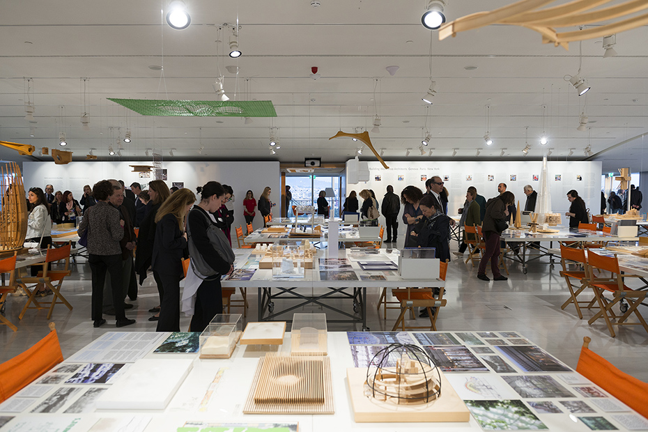 Φωτογραφία που δείχνει κόσμο να στέκεται και να κοιτάει τραπέζια στα οποία υπάρχουν σχέδια, υπομνήματα, εικόνες και μακέτες κτηρίων 