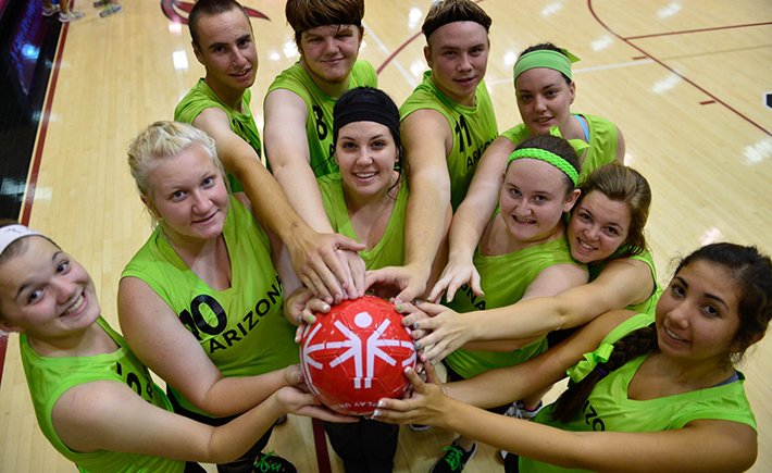 Ομαδική φωτογραφία μιας ομάδας των Special Olympics, τα μέλη της οποίας απλώνουν το χέρι τους για να αγγίξουν μια μπάλα