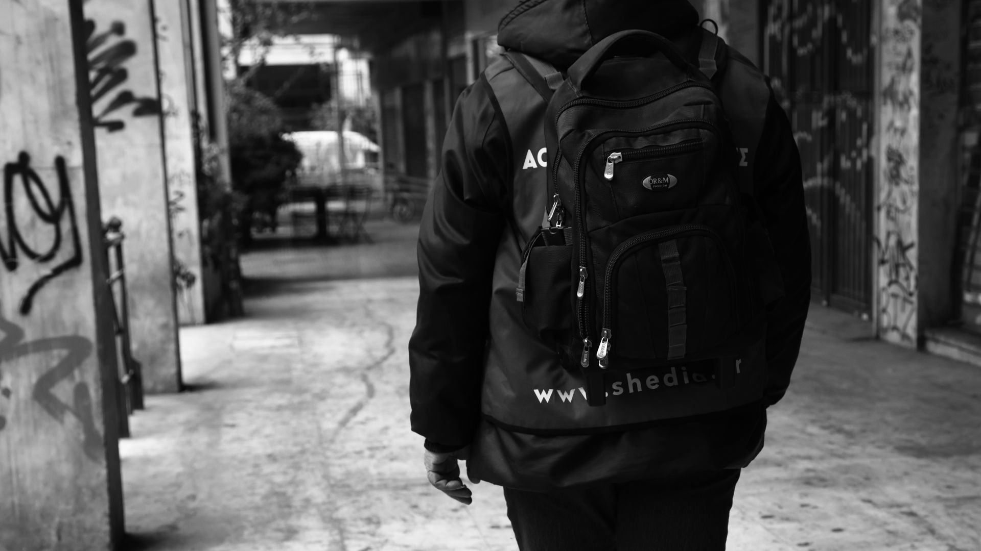 Ασπρόμαυρη φωτογραφία με ένα άτομο που φοράει σακίδιο πλάτης και μπουφάν και περπατάει σε μια περιοχή καλυμμένη με γκράφιτι