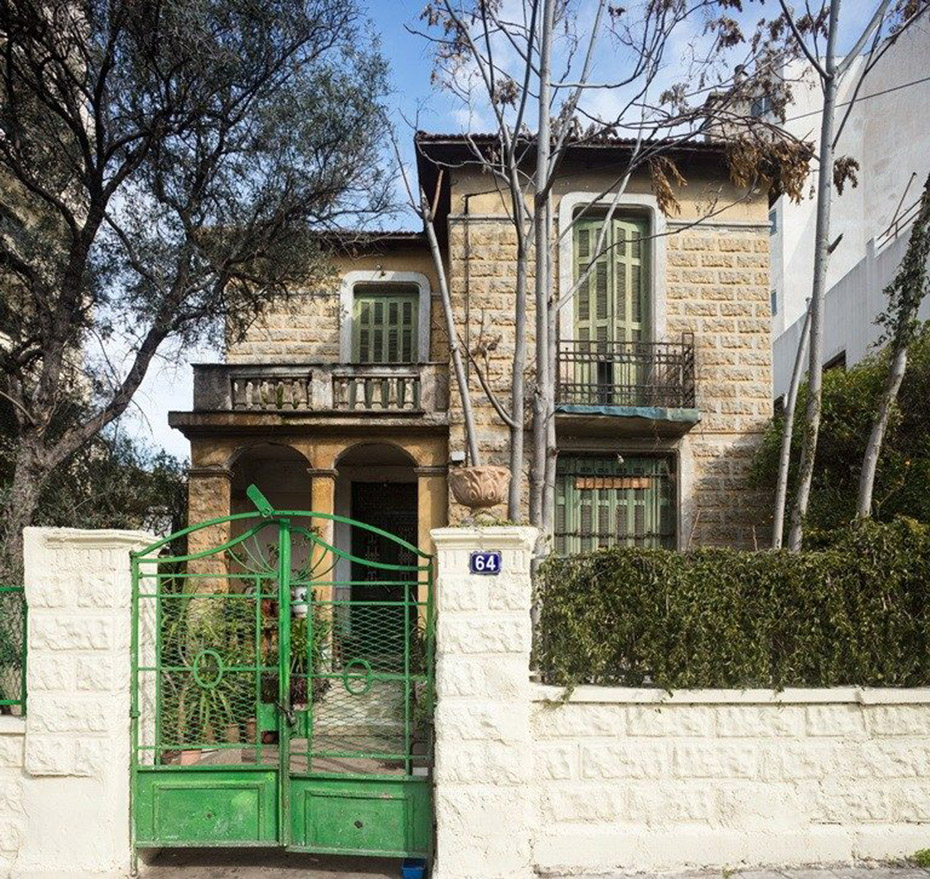 Ένα μπεζ, πέτρινο σπίτι με πράσινα παράθυρα και πράσινη εξώπορτα  