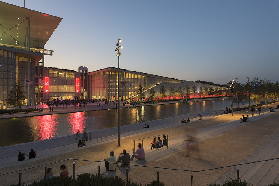 Φωτογραφία που δείχνει ανθρώπους να κάθονται σε σκαλιά και να κοιτάνε μια λίμνη και ένα μεγάλο γυάλινο κτήριο που υπάρχουν μπροστά τους 