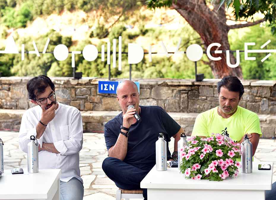 Ο Αντρέας Δρακόπουλος, Πρόεδρος του Ιδρύματος Σταύρος Νιάρχος, κάθεται στην κεντρική πλατεία ενός χωριού μαζί με άλλους ανθρώπους και μιλάει κρατώντας ένα μικρόφωνο