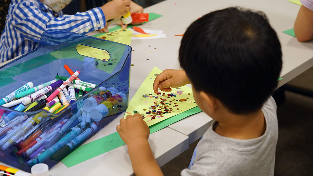 Ένα μικρό αγόρι χρησιμοποιεί γκλίτερ και μαρκαδόρους για να κάνει χειροτεχνίες