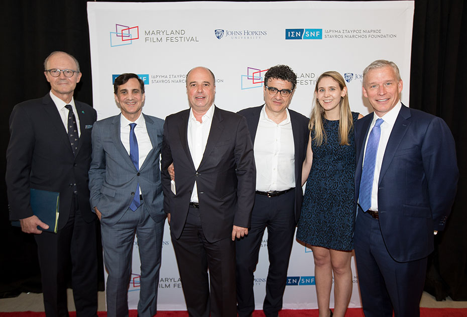 Ο Αντρέας Δρακόπουλος, Πρόεδρος του Ιδρύματος Σταύρος Νιάρχος βγάζει μια αναμνηστική φωτογραφία μαζί με άλλα μέλη του John Hopkins University και του Maryland Film Festival μπροστά από ένα μεγάλο banner το οποίο έχει τα logo του Ιδρύματος Σταύρος Νιάρχος, του John Hopkins University και του MARYLAND FILM FESTIVAL 