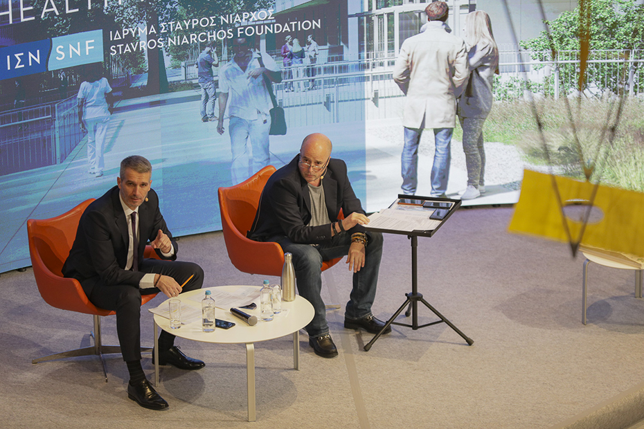 Ο Αντρέας Δρακόπουλος, Πρόεδρος του Ιδρύματος Σταύρος Νιάρχος κάθεται με έναν άλλον άντρα στη σκηνή 