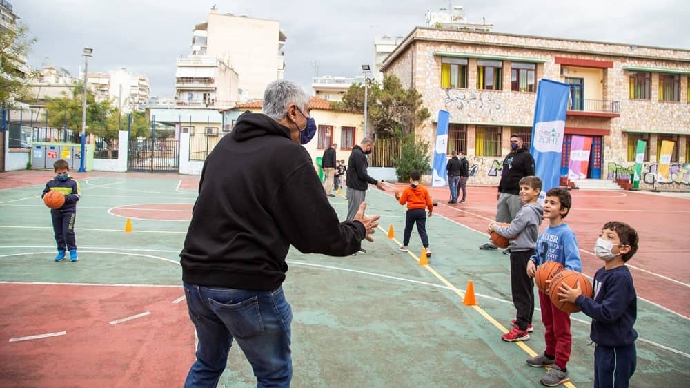 Άντρες και αγοράκια παίζουν μπάσκετ σε γήπεδο σχολείου