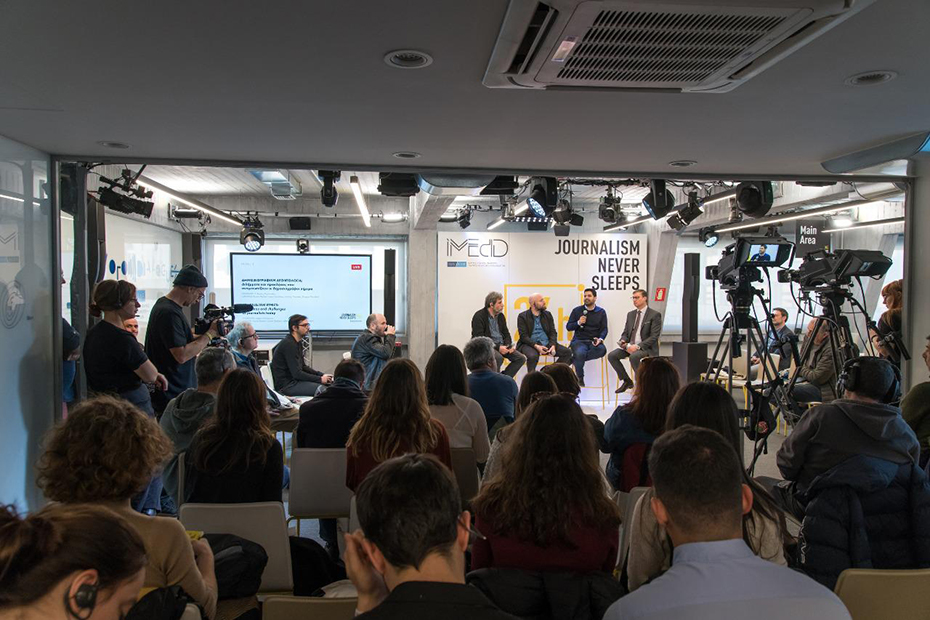 Φωτογραφία που δείχνει το κοινό που παρακολουθεί τους τέσσερεις άντρες που βρίσκονται στη σκηνή και μιλάνε