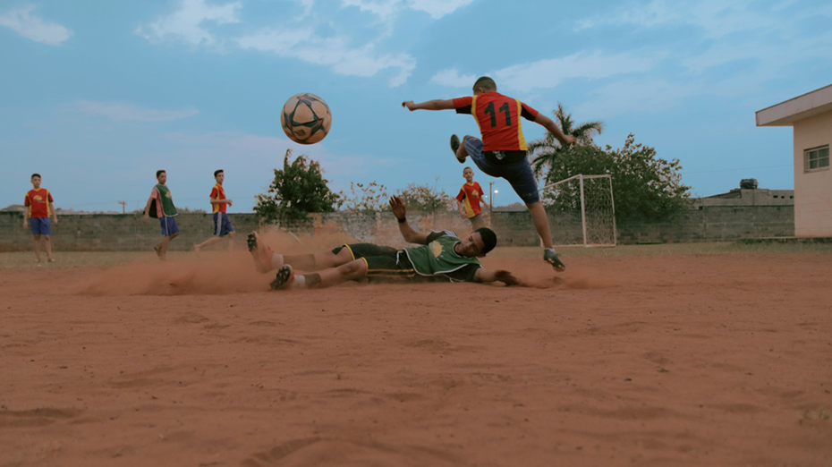 Μια ομάδα παιδιών παίζει ποδόσφαιρο και ένα αγόρι είναι πεσμένο στο πάτωμα ενώ ο αντίπαλός του πηδάει από πάνω του 