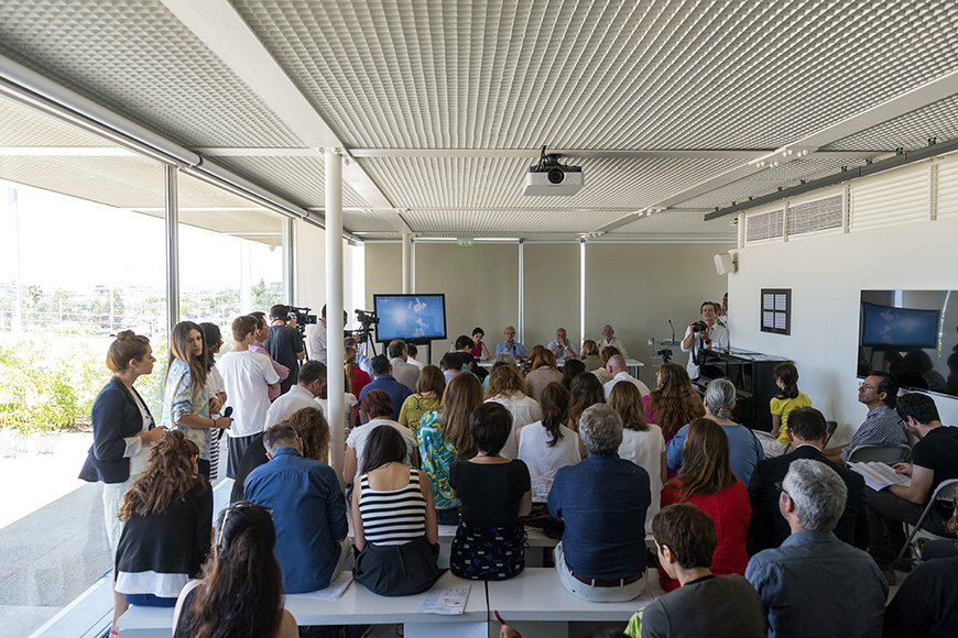 Άνθρωποι κάθονται και παρακολουθούν μια ομιλία μέσα σε μία άιθουσα 