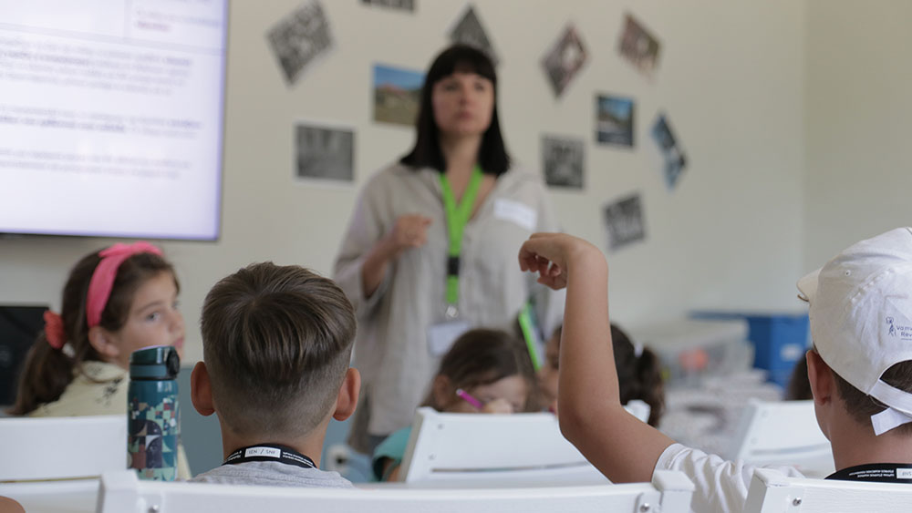 Πέντε παιδιά παρακολουθούν ένα εκπαιδευτικό πρόγραμμα και ένα αγοράκι σηκώνει το χέρι του 