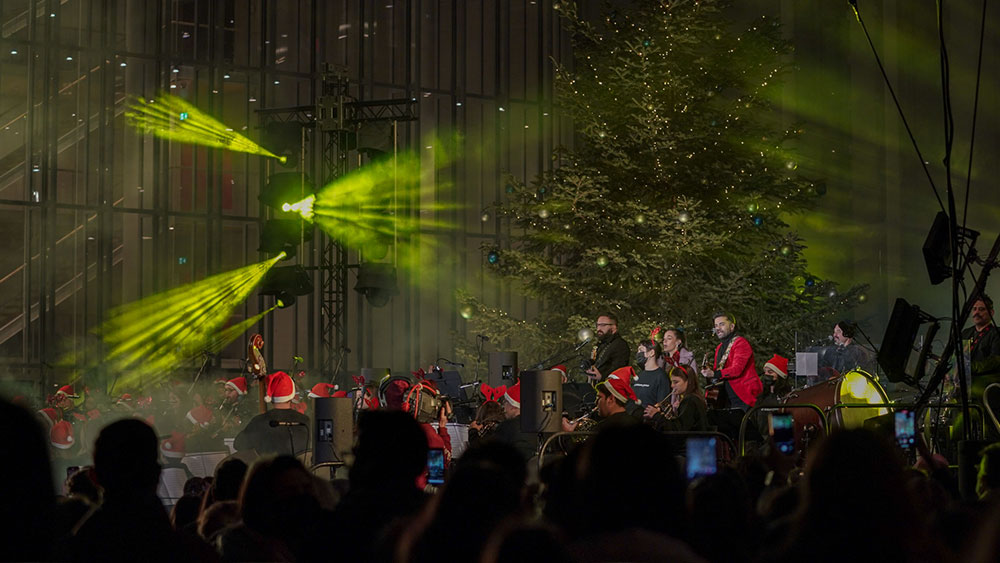 Μια μπάντα και μια ορχήστρα παίζουν μπροστά από ένα στολισμένο δέντρο στο Κέντρο Πολιτισμού Ίδρυμα Σταύρος Νιάρχος