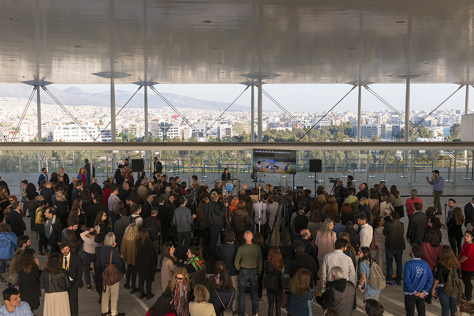 Μακρινή φωτογραφία που δείχνει πλήθος ανθρώπων να στέκονται όρθιοι και να παρακολουθούν μια ομιλία