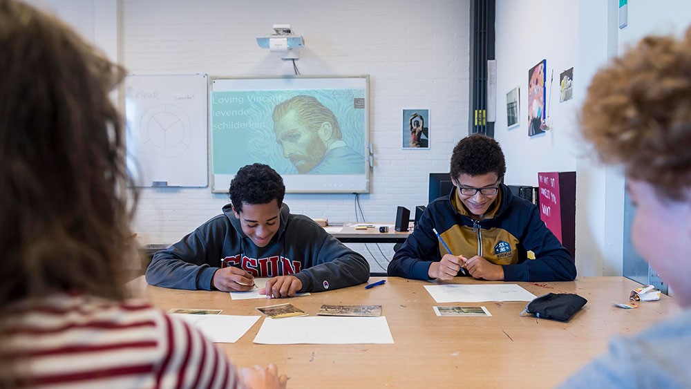 Δύο χαμογελαστοί μαθητές κάθονται σε ένα τραπέζι και δουλεύουν πάνω σε εργασίες σχετικές με τον Βαν Γκογκ