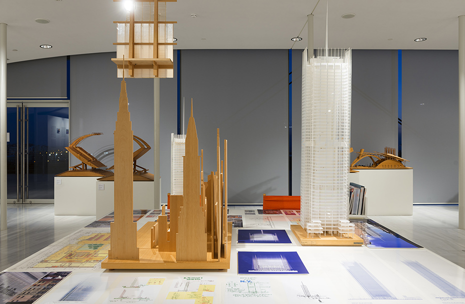 Δύο μακέτες που δείχνουν ψηλά κτήρια τοποθετημένες πάνω σε ένα τραπέζι και γύρω τους υπάρχουν τα σχέδια και οι σημειώσεις που τις συνοδεύουν