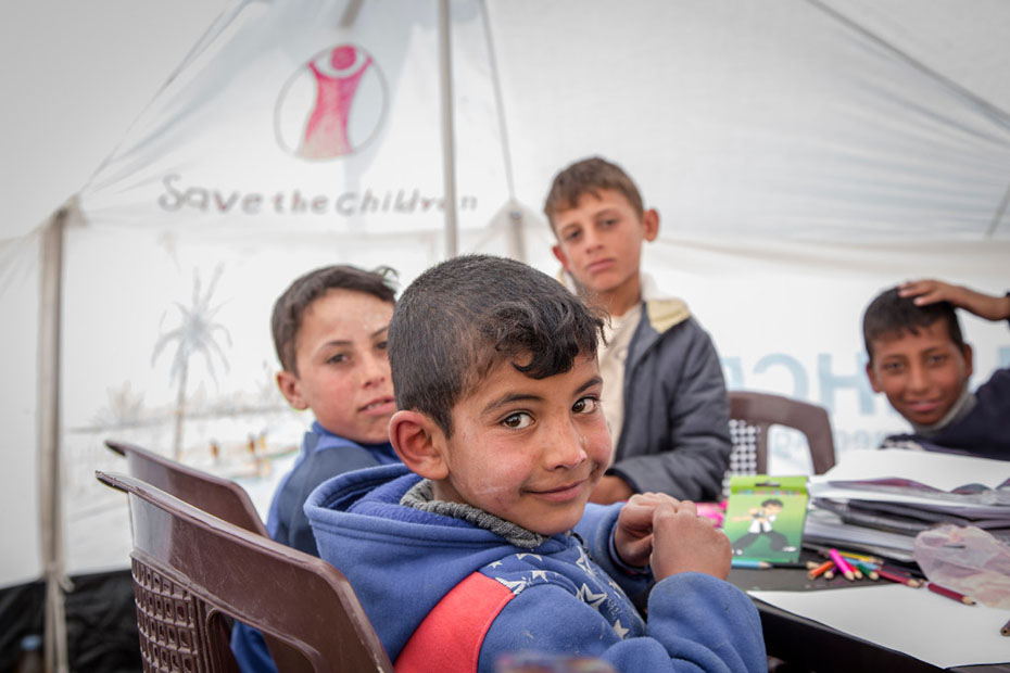 Τέσσερα μικρά αγόρια κάθονται γύρω από ένα τραπέζι και ζωγραφίζουν και ποζάρουν για μια φωτογραφία
