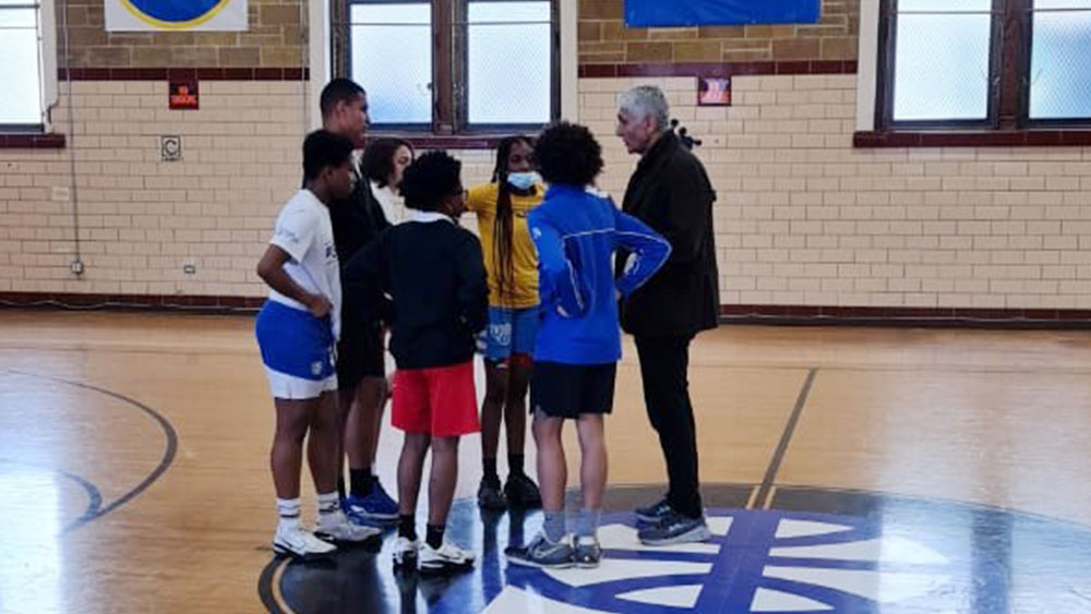 Πέντε παιδιά στέκονται σε κύκλο γύρω από έναν προπονητή σε ένα γήπεδο μπάσκετ