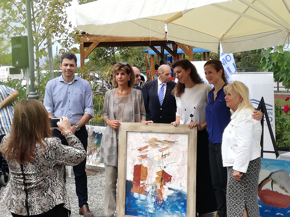 Μια γυναίκα φωτογραφίζει τα μέλη του Ιδρύματος Σταύρος Νιάρχος και του Κέντρου Αποκατάστασης Παιδιών με Αναπηρία Αττικής, τα οποία κρατούν έναν πίνακα ζωγραφικής