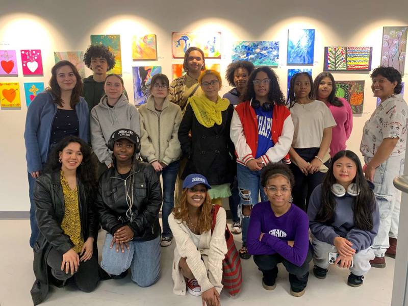 A group of young people smiling and posing for a photo in front of colorful art pieces.