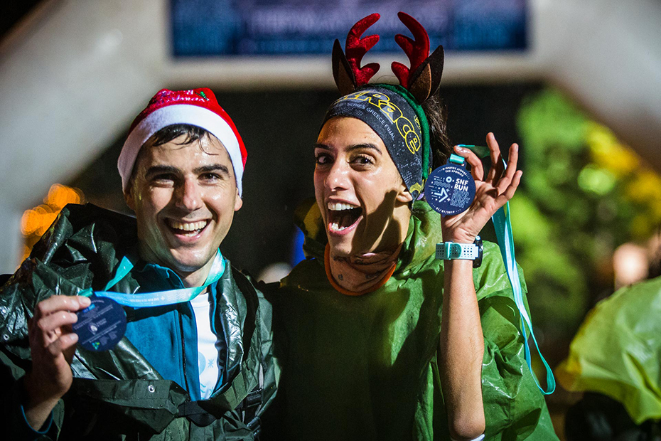 Ένας άνδρας και μια γυναίκα με χριστουγεννιάτικο καπέλο και καπέλο ταράνδου χαμογελούν και κρατούν ψηλά τα μετάλλιά τους