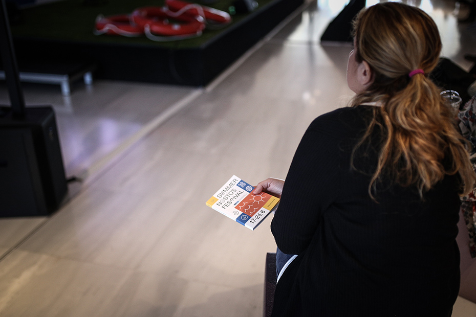 Μια γυναίκα στο κοινό κρατάει το φυλλάδιο του Summer Nostos Festival