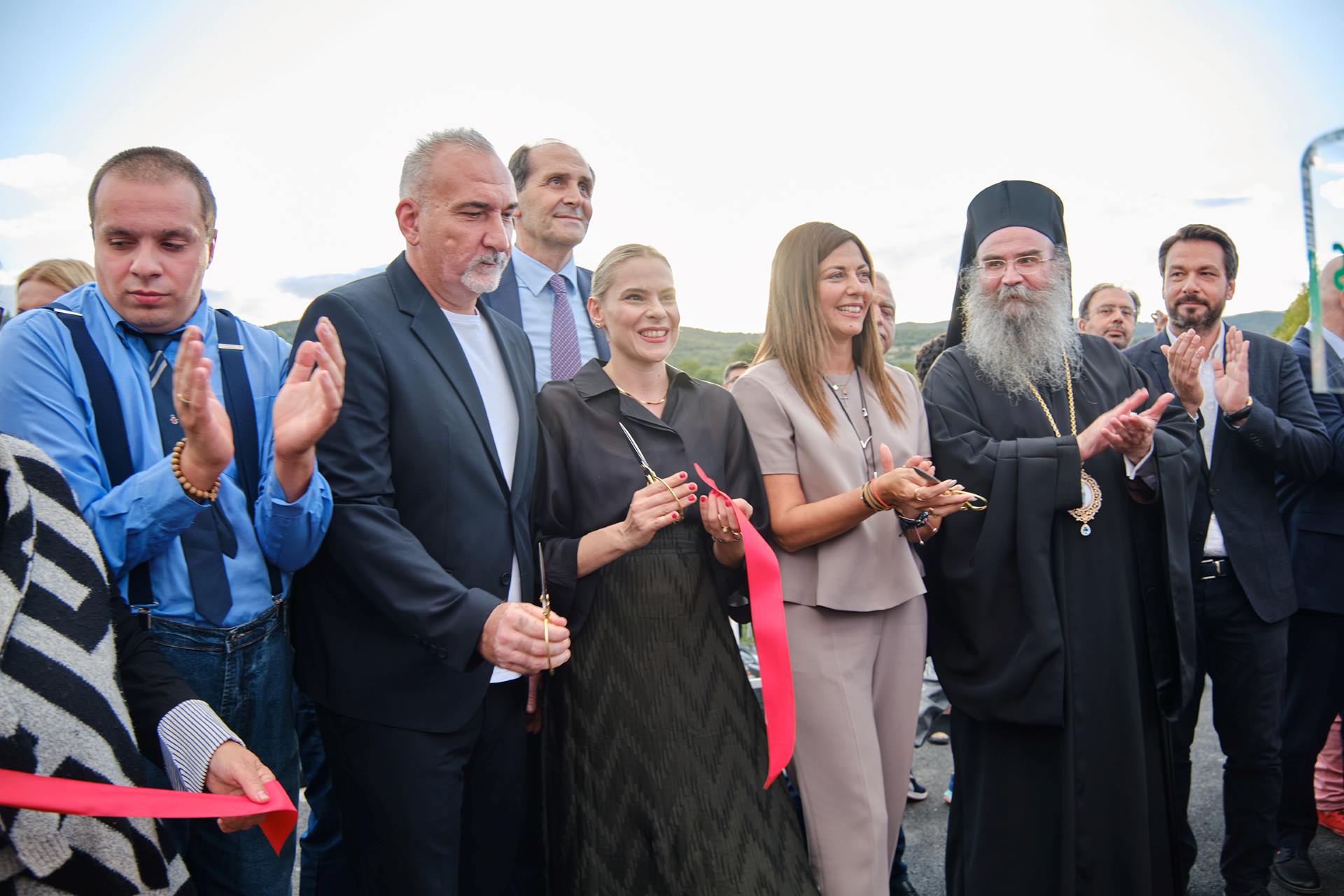 Μια ομάδα ατόμων κόβει μια κορδέλα, γιορτάζοντας μια σημαντική περίσταση με χαμόγελα και ενθουσιασμό.