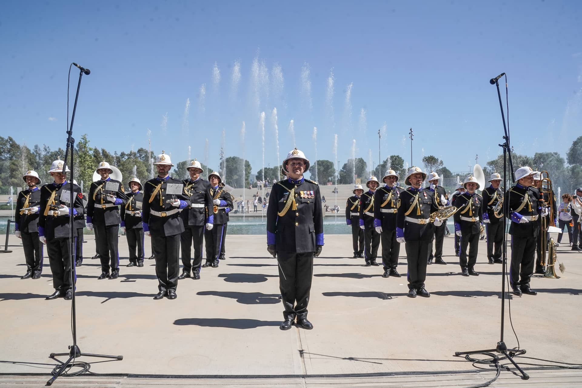 Μια μπάντα με στρατιωτικές στολές στέκεται προσοχή μπροστά από ένα σιντριβάνι στο κανάλι του Κέντρου Πολιτισμού Ίδρυμα Σταύρος Νιάρχος.