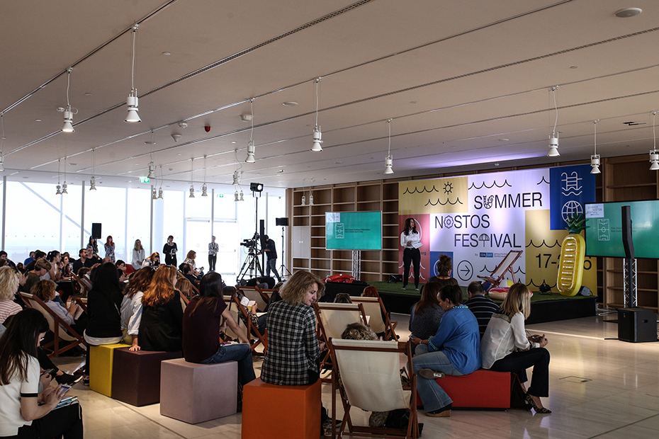 Το κοινό παρακολουθεί μια γυναίκα να μιλάει στη σκηνή του Summer Nostos Festival