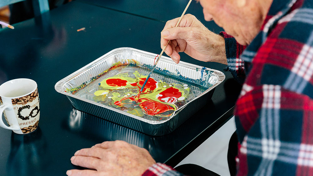 Ένας ηλικιωμένος άντρας μετακινεί μπογιά σε ένα ταψί με ένα πινέλο