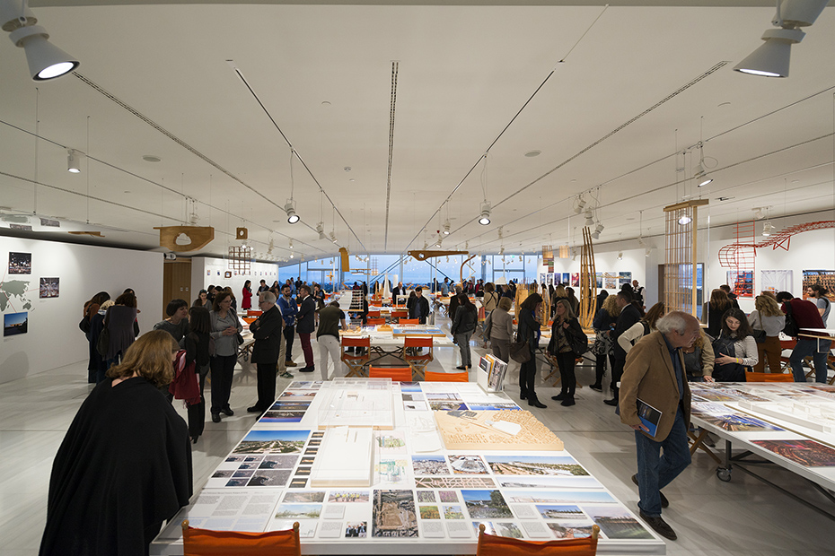 Μακρινή φωτογραφία που δείχνει κόσμο να στέκεται και να κοιτάει τραπέζια στα οποία υπάρχουν σχέδια, υπομνήματα, εικόνες και μακέτες κτηρίων 