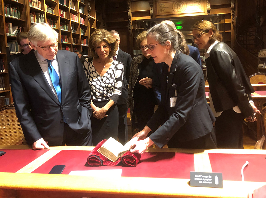 Μια γυναίκα δείχνει στα μέλη ένα παλιό βιβλίο που αποτελεί μέρος μιας συλλογής στη βιβλιοθήκη