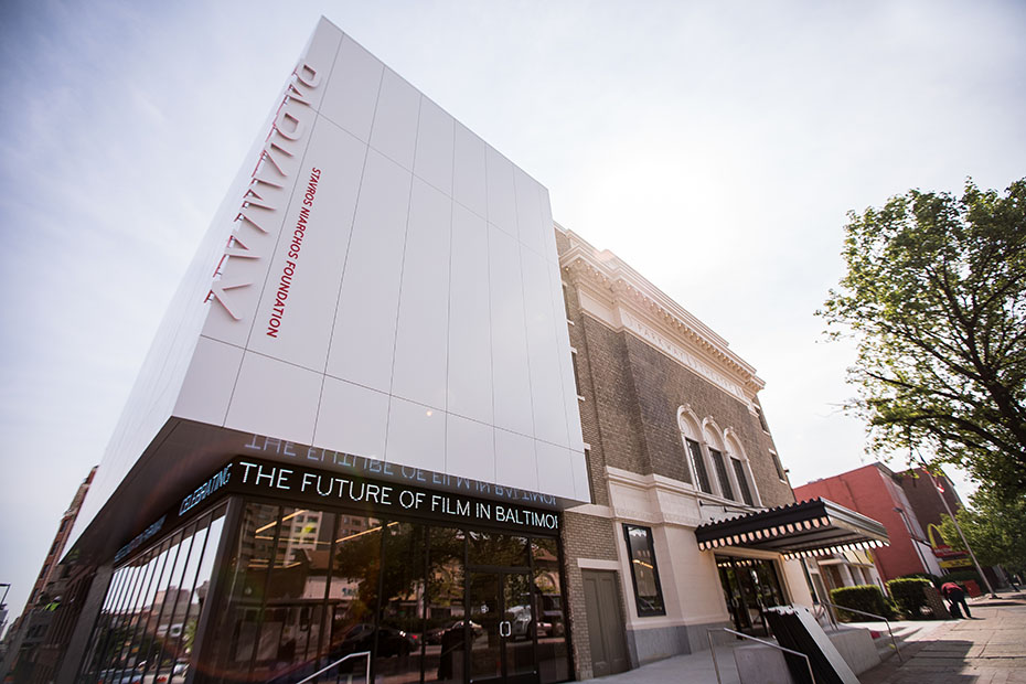 Φωτογραφία που δείχνει την εξωτερική όψη ενός κτηρίου το οποίο στη βάση του έχει παντού τζαμαρίες ενώ στους ορόφους εξωτερικά μοιάζει με ένα μεγάλο κουτί και γράφει PARKWAY STAVROS NIARCHOS FOUNDATION THE FUTURE OF FILM IN BALTIMOR