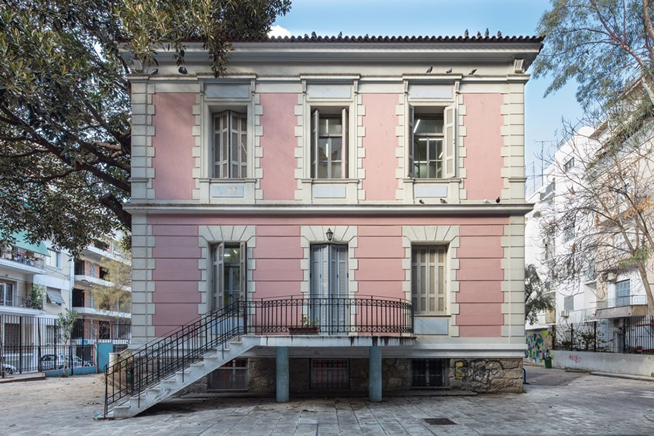 Ένα ροζ, διώροφο κτίριο με σκάλες που οδηγούν στην είσοδο