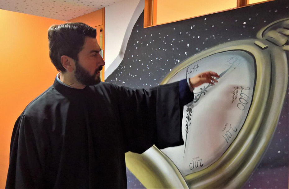 Ένας ιερέας κοιτάει έναν πίνακα με ένα μεγάλο ρολόι και δείχνει με το χέρι του στον πίνακα 