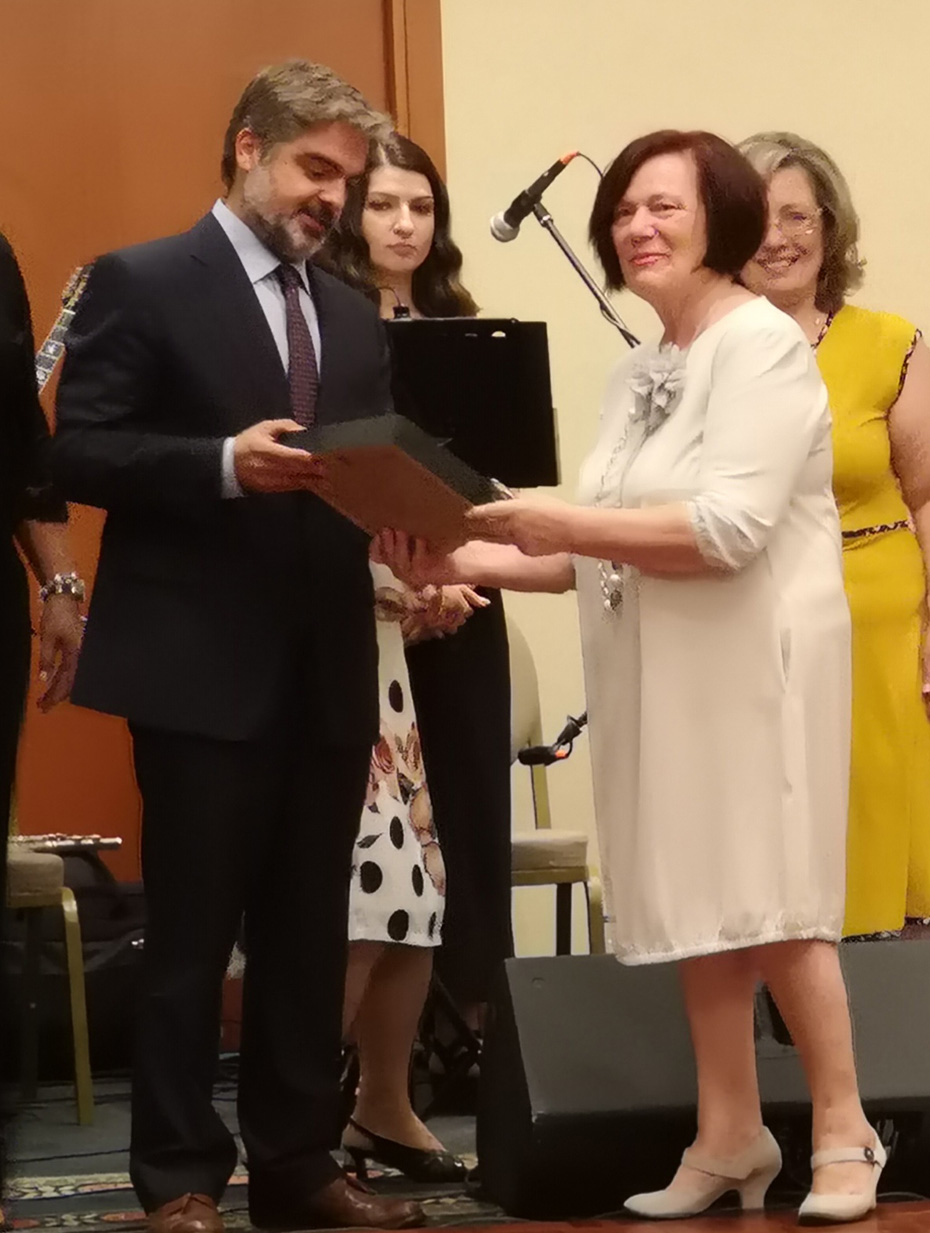 Μια γυναίκα απονέμει βραβείο σε έναν άνδρα μπροστά σε άλλους ανθρώπους