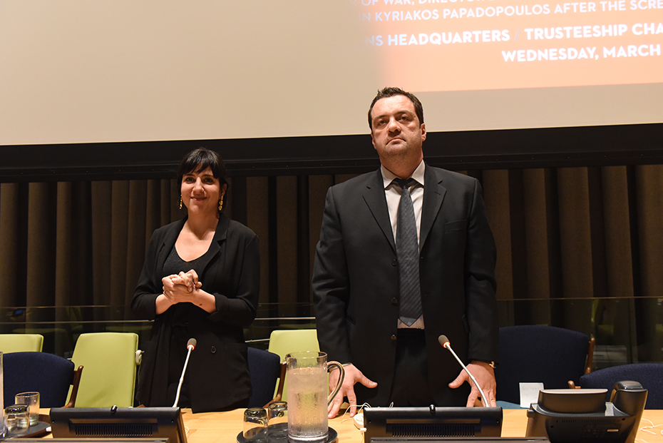 Δύο άτομα στέκονται μπροστά από την οθόνη που προβάλλει το ντοκιμαντέρ στα Ηνωμένα Έθνη