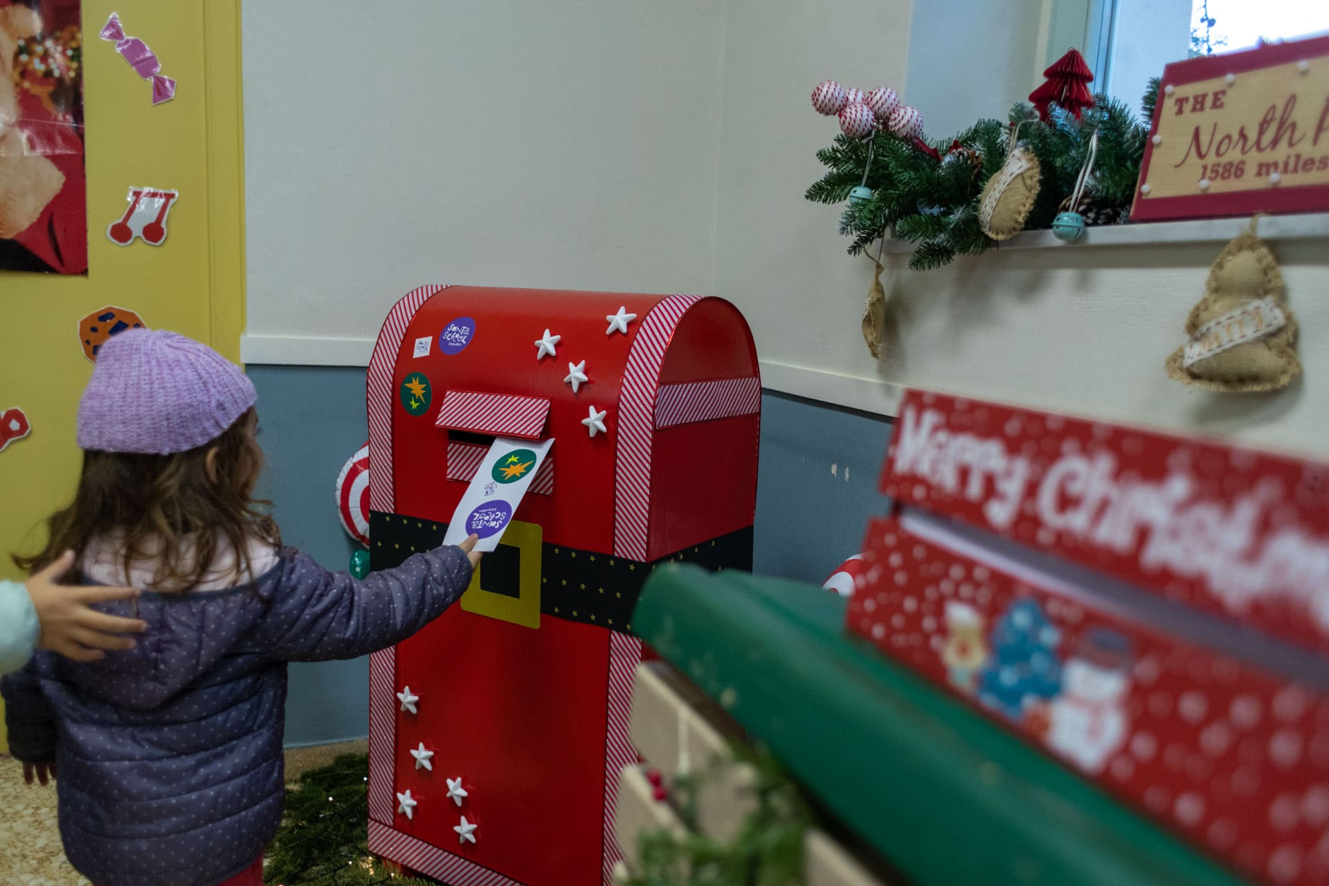 Παιδί που στέλνει ένα Χριστουγεννιάτικο γράμμα μέσα σε ένα κόκκινο ταχυδρομικό κουτί σε ένα δωμάτιο.