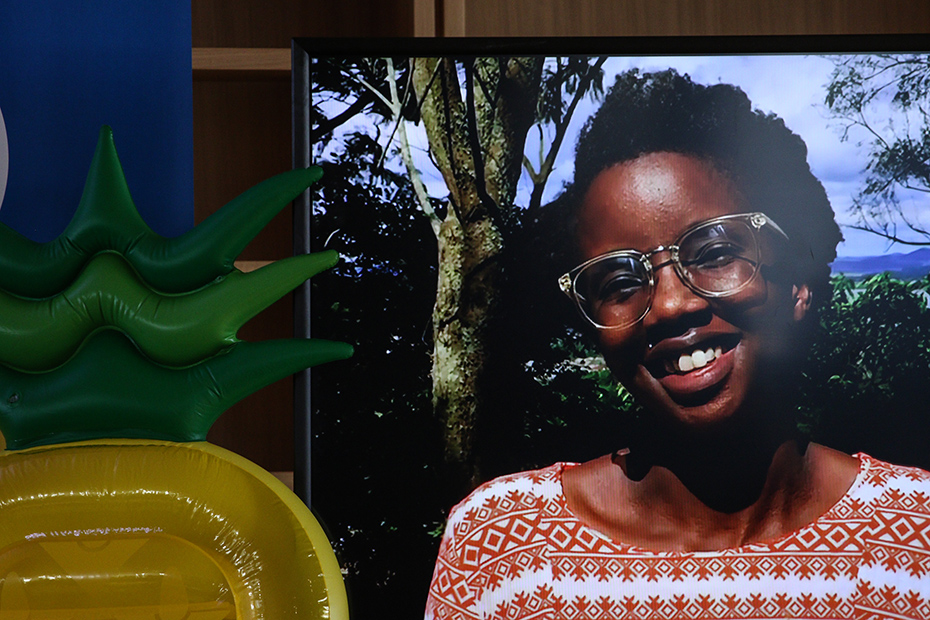 Μια οθόνη δείχνει την εικόνα μιας χαμογελαστής γυναίκας με γυαλιά, δίπλα σε έναν φουσκωτό ανανά.