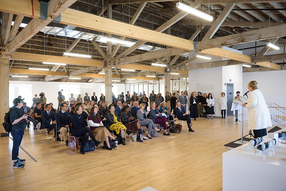 Μια γυναίκα δίνει μια ομιλία σε καθισμένο κοινό μέσα σε ένα χώρο τεχνών