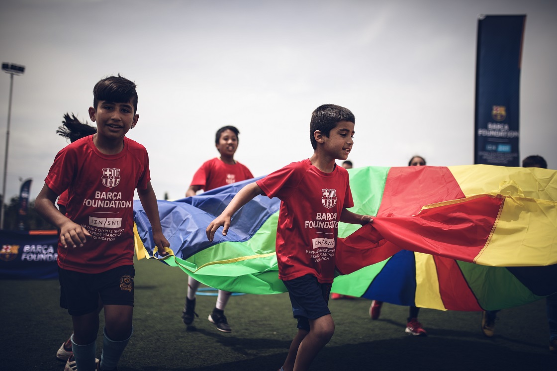 Μικρά παιδιά τρέχουν κρατώντας ένα πολύχρωμο σεντόνι σε ένα γήπεδο ποδοσφαίρου