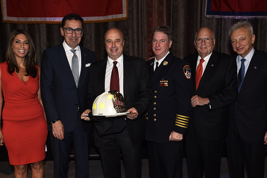 Ο Αντρέας Δρακόπουλος, Πρόεδρος του Ιδρύματος Σταύρος Νιάρχος, στέκεται για μια αναμνηστική φωτογραφία μαζί με άλλους τέσσερις άντρες και μια γυναίκα κρατώντας το δώρο τιμής που του αποδόθηκε, ένα καπέλο πυροσβέστη