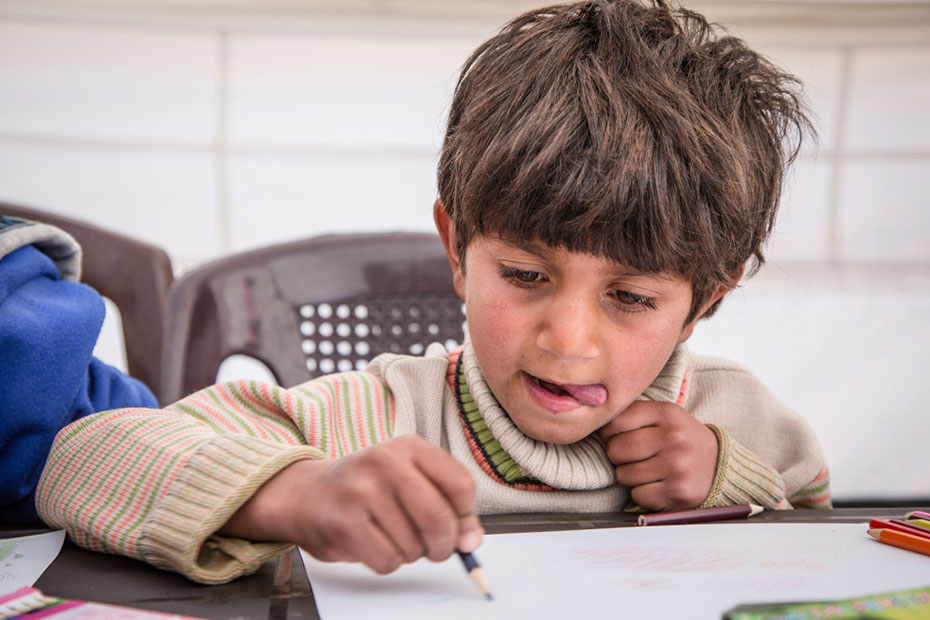 Ένα μικρό αγοράκι κάθεται στο τραπέζι και ζωγραφίζει με τη γλώσσα έξω