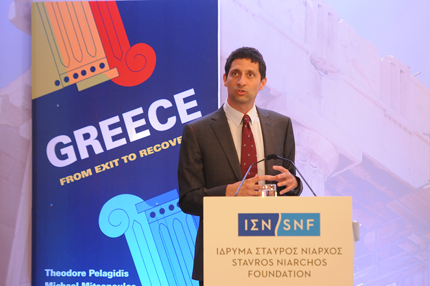Ένας άντρας βγάζει λόγο στο βήμα του Ιδρύματος Σταύρος Νιάρχος και πίσω του υπάρχει ένα banner το οποίο γράφει GREECE FROM EXIT TO RECOIVERY?