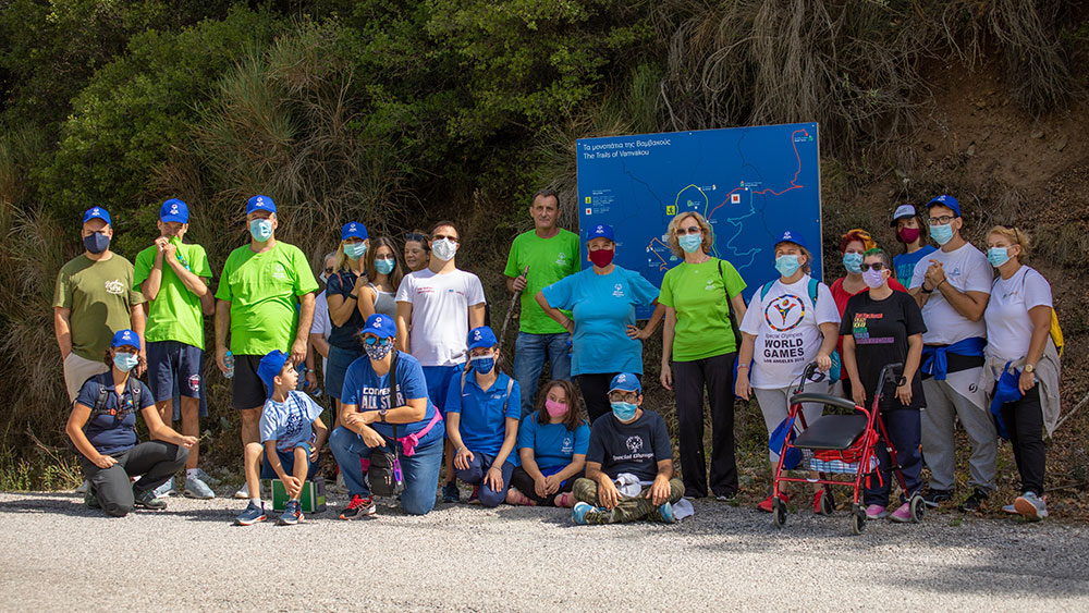 Οι αθλητές των Special Olympics Hellas και οι γονείς τους ποζάρουν για μια φωτογραφία μπροστά από μια πινακίδα που δείχνει τα μονοπάτια της Βαμβακού