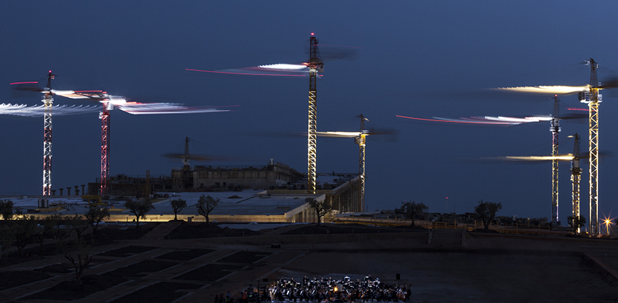 Φωτογραφία που δείχνει έξι γερανούς τοποθετημένους μέσα σε ένα εργοτάξιο να είναι φωτισμένοι τη νύχτα